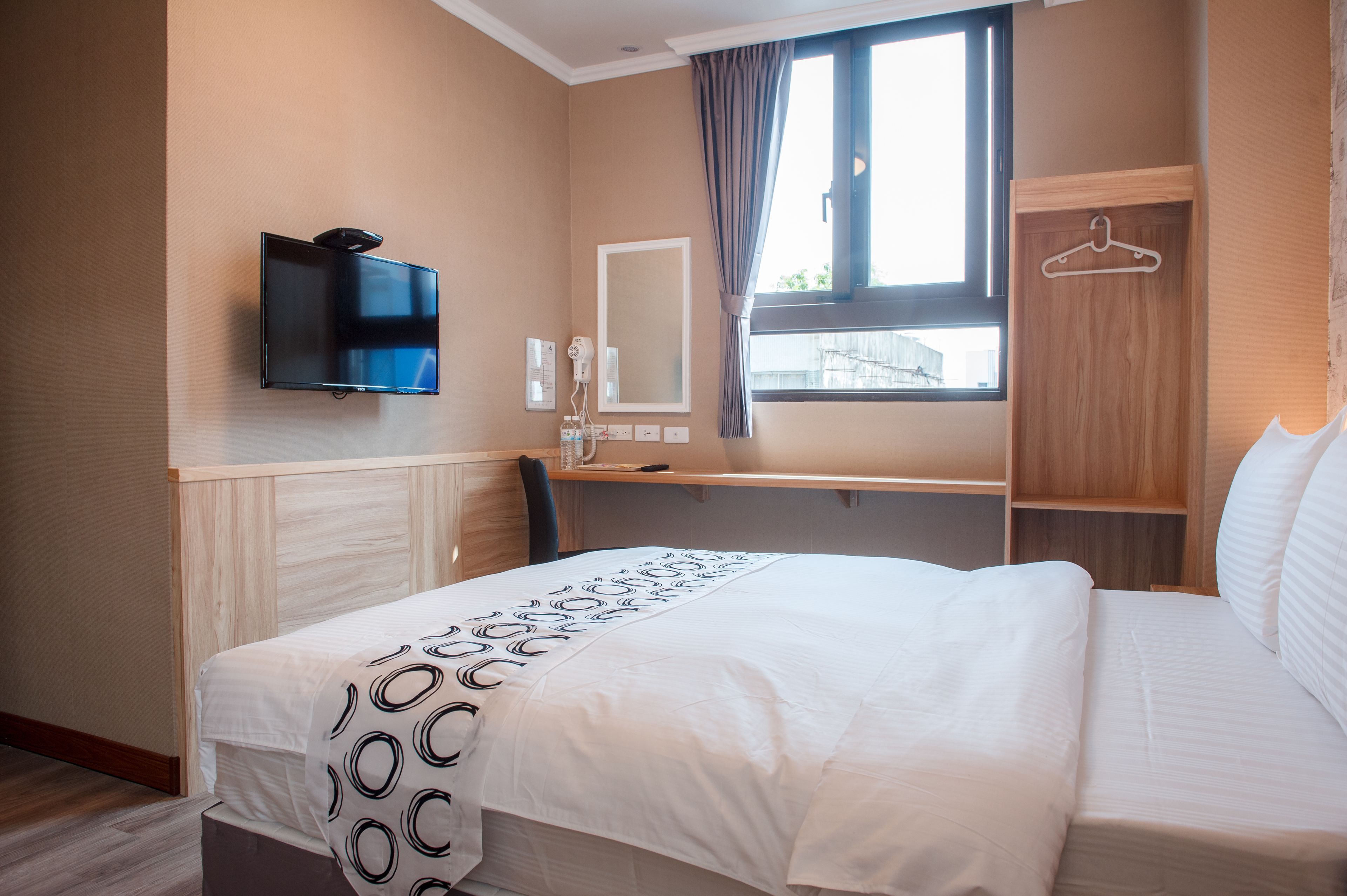 A hotel room with a bed, a desk, a TV, a mirror, and a window with curtains.