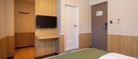 A hotel room with a bed, a mounted TV, a door with a lock, and a wall-mounted thermostat.