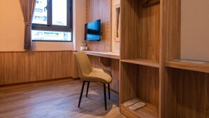 Una habitación con un escritorio de madera, una silla, un televisor montado en la pared y una ventana con cortinas.