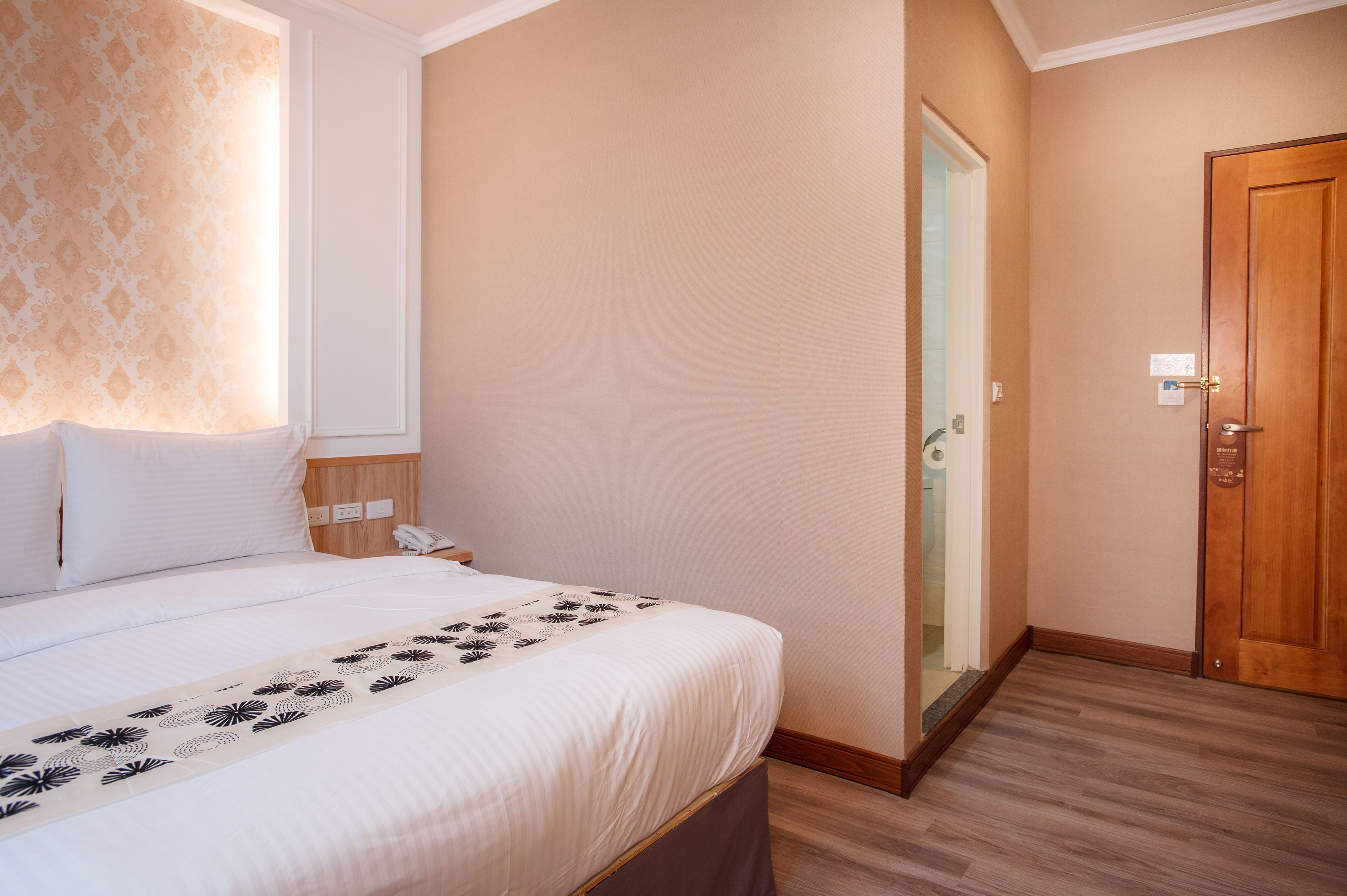 A hotel room with a bed, bedside table, and a wooden door.