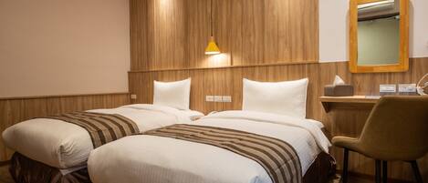 Quarto de hotel com duas camas, cabeceira de madeira, escrivaninha com cadeira e espelho.