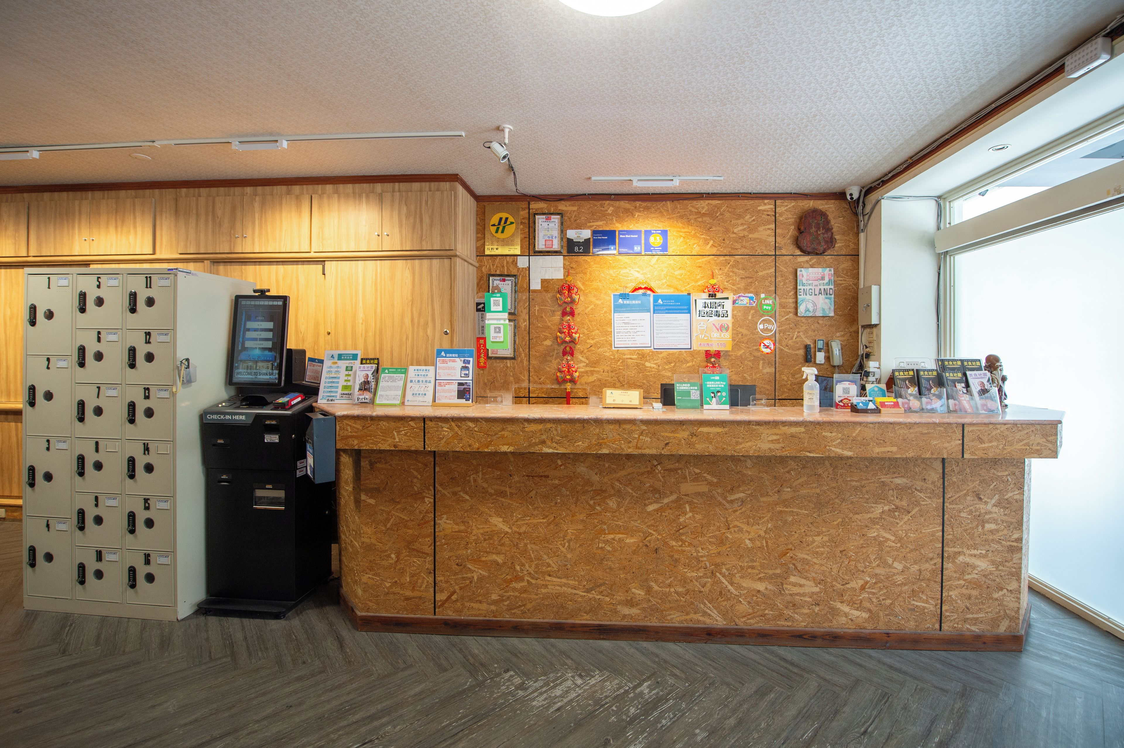 Ein Hotel-Rezeptionsbereich mit einem Holzbüro, einer digitalen Check-in-Kiosk und einer Reihe nummerierter Schließfächer.