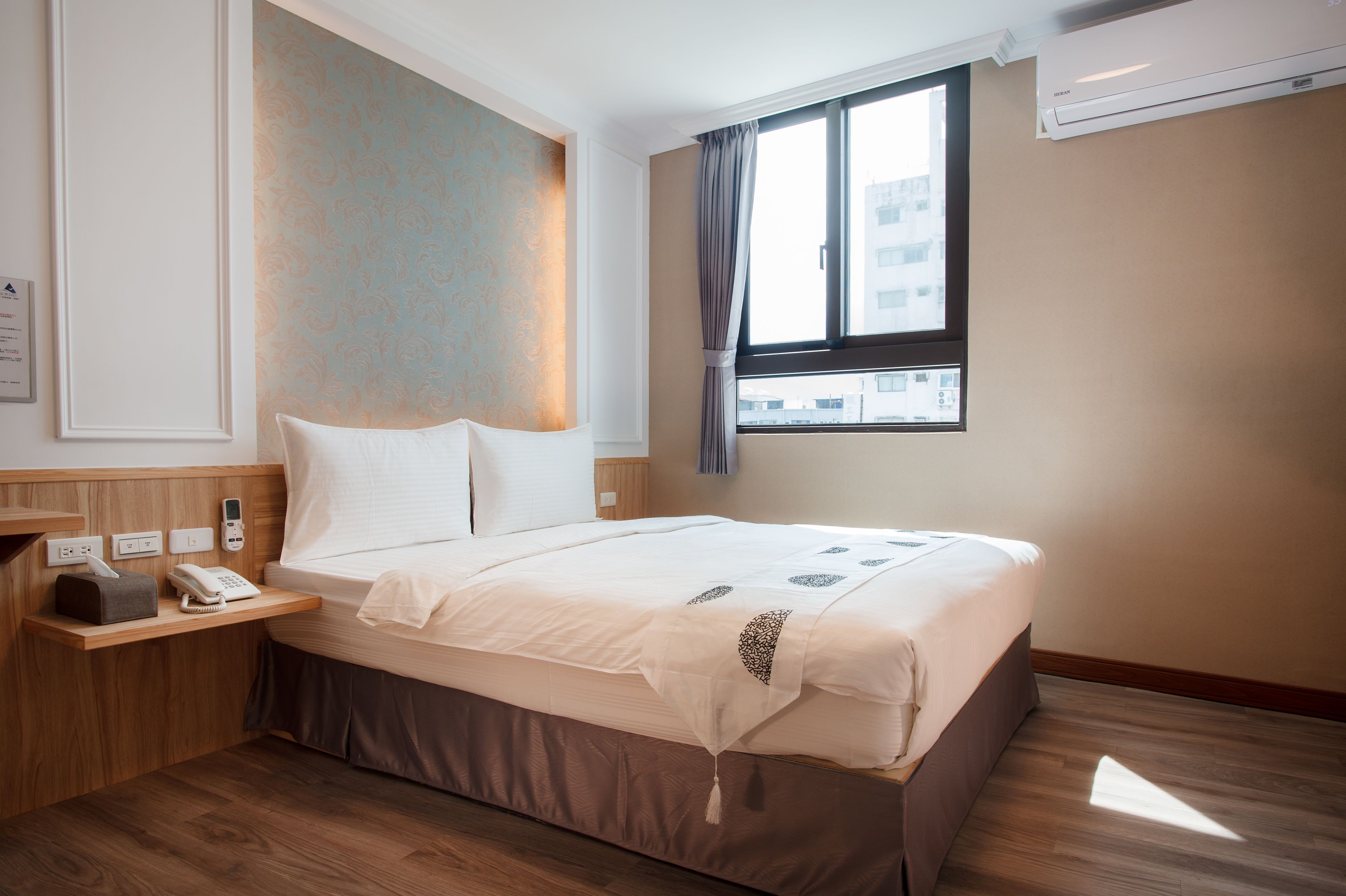 A hotel room with a bed, bedside table, and a window with curtains.