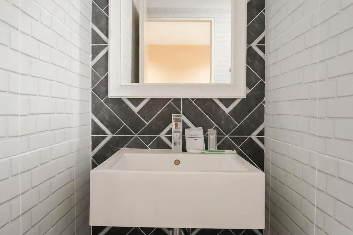 A bathroom with a white sink, a mirror, and black and white patterned tiles.