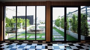 A room with large sliding glass doors leading to a garden with a fountain, a checkered floor, and a view of the cityscape. - The O-Zone Airport Inn (Bangkok)