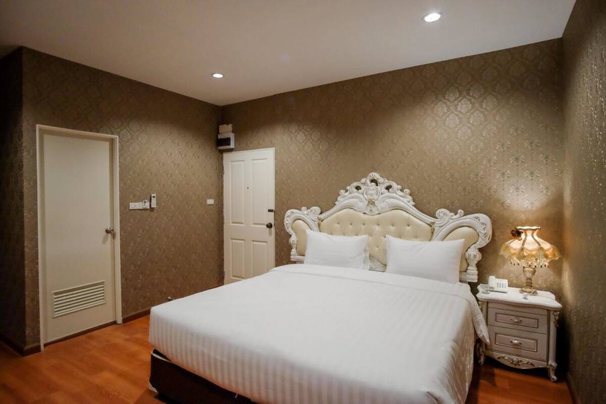 A bedroom with a large bed, a nightstand with a lamp, and a door.