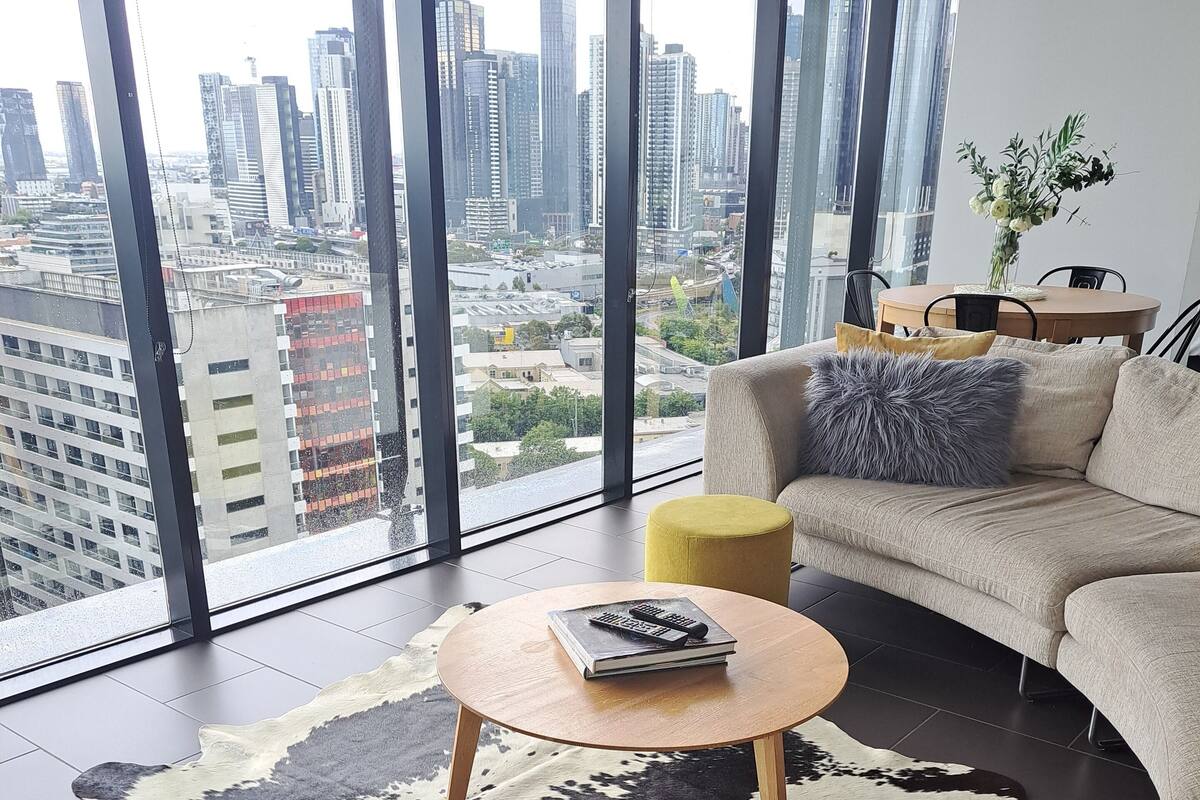 A modern living room with a large city view, a leather rug, a round coffee table, and a sofa with cushions.