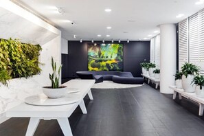 A modern lobby with a marble wall, a large abstract painting, a dark sofa, and potted plants. - Xanadu Apartments (Southbank)