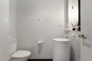 A modern bathroom with a toilet, sink, and mirror. - Xanadu Apartments (Southbank)