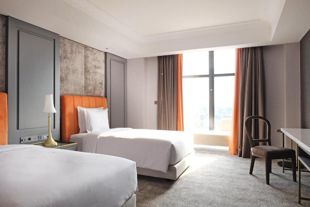A hotel room with two beds, a desk, and a chair.