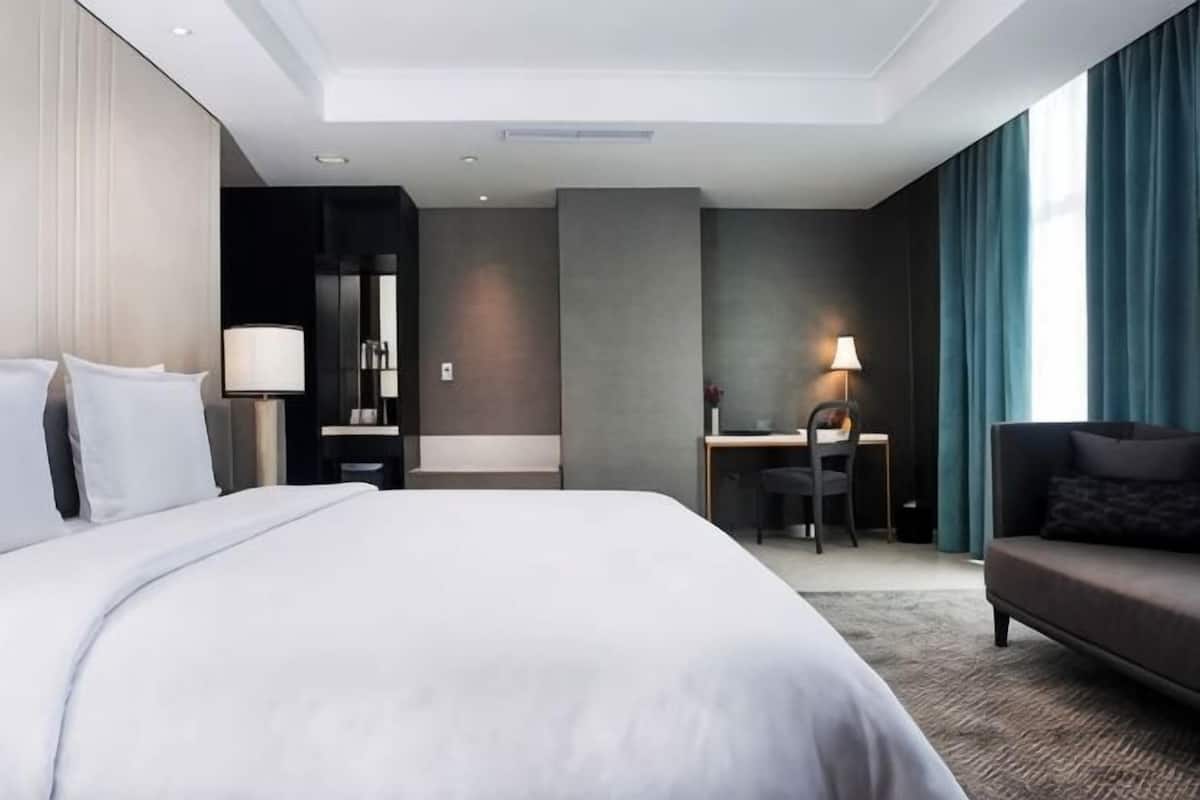 A modern hotel room with a large bed, a desk, a sofa, and a view of the city.