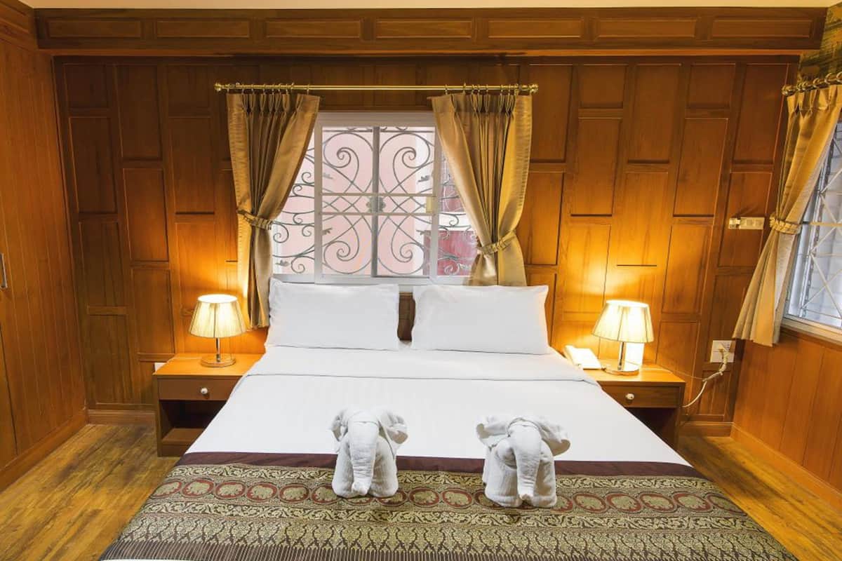 A hotel room with a large bed, wooden paneling, two bedside lamps, and two plush toys on the bed.