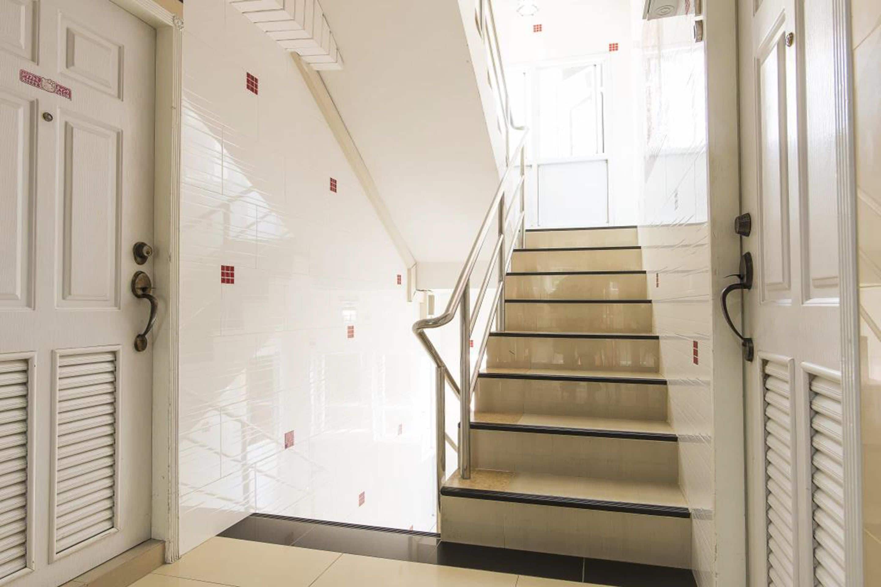 A staircase with a handrail, white doors with latches, and a tiled floor.