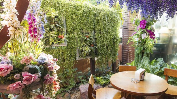 A garden patio with a round wooden table and chairs, surrounded by lush greenery and various flowering plants. - Orchid Resort (Bangkok)