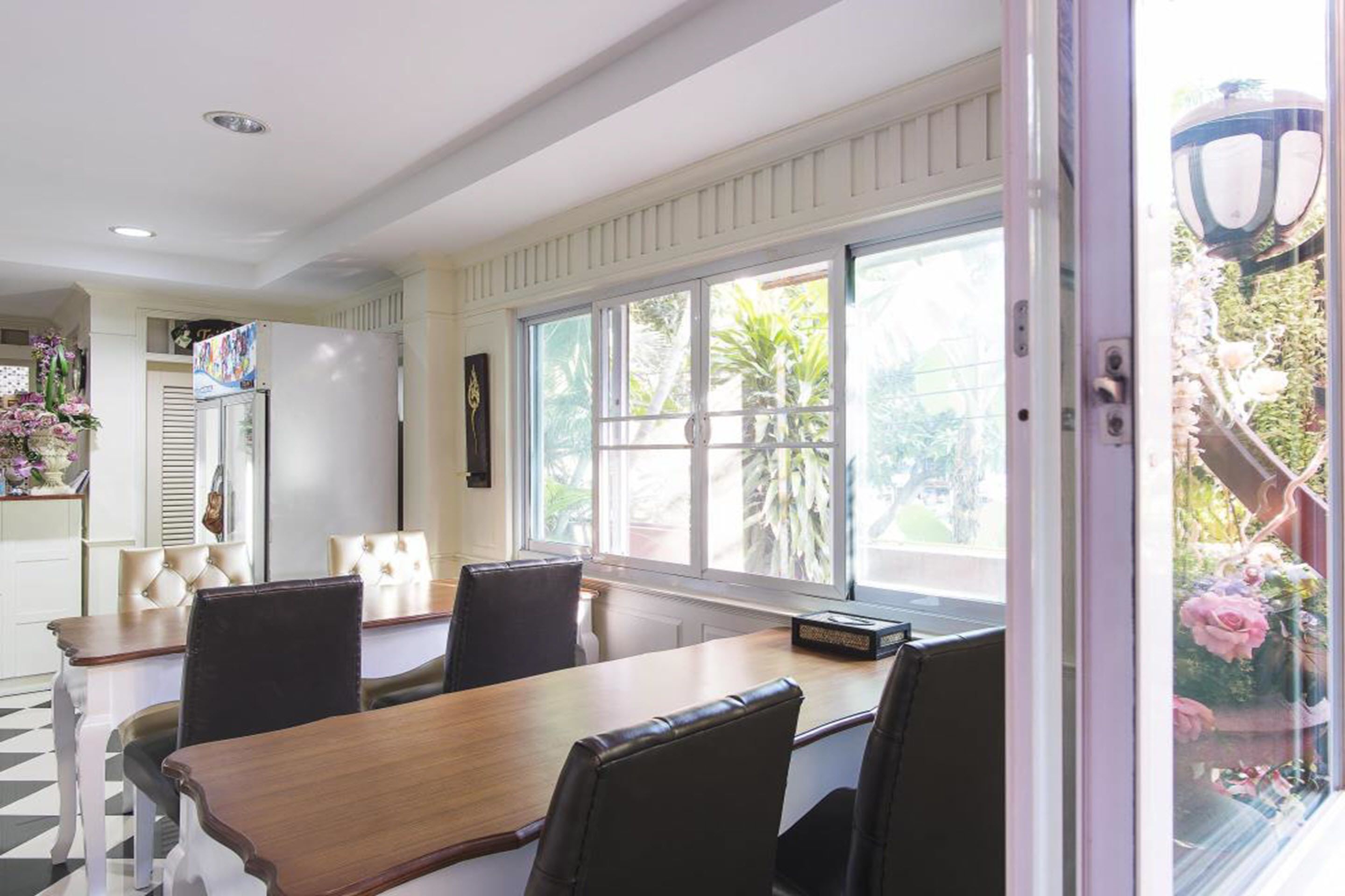 Un comedor con una gran mesa de madera, sillas negras y vistas a un jardín a través de amplios ventanales.