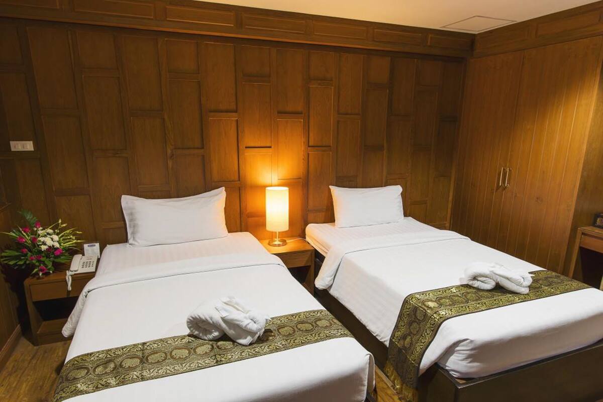 A hotel room with two single beds, wooden paneling on the walls, a bedside lamp, a telephone, and a flower arrangement.