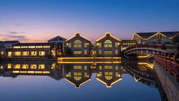 A waterfront hotel with illuminated facades reflecting on the water, a bridge, and a stone balustrade. - Lin Yin Art Hotel Shanghai PVG Airport Disneyland Free Shuttle (Shanghai)