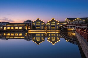 A waterfront hotel with illuminated facades reflecting on the water, a bridge, and a stone balustrade. - Lin Yin Art Hotel Shanghai PVG Airport Disneyland Free Shuttle (Shanghai)