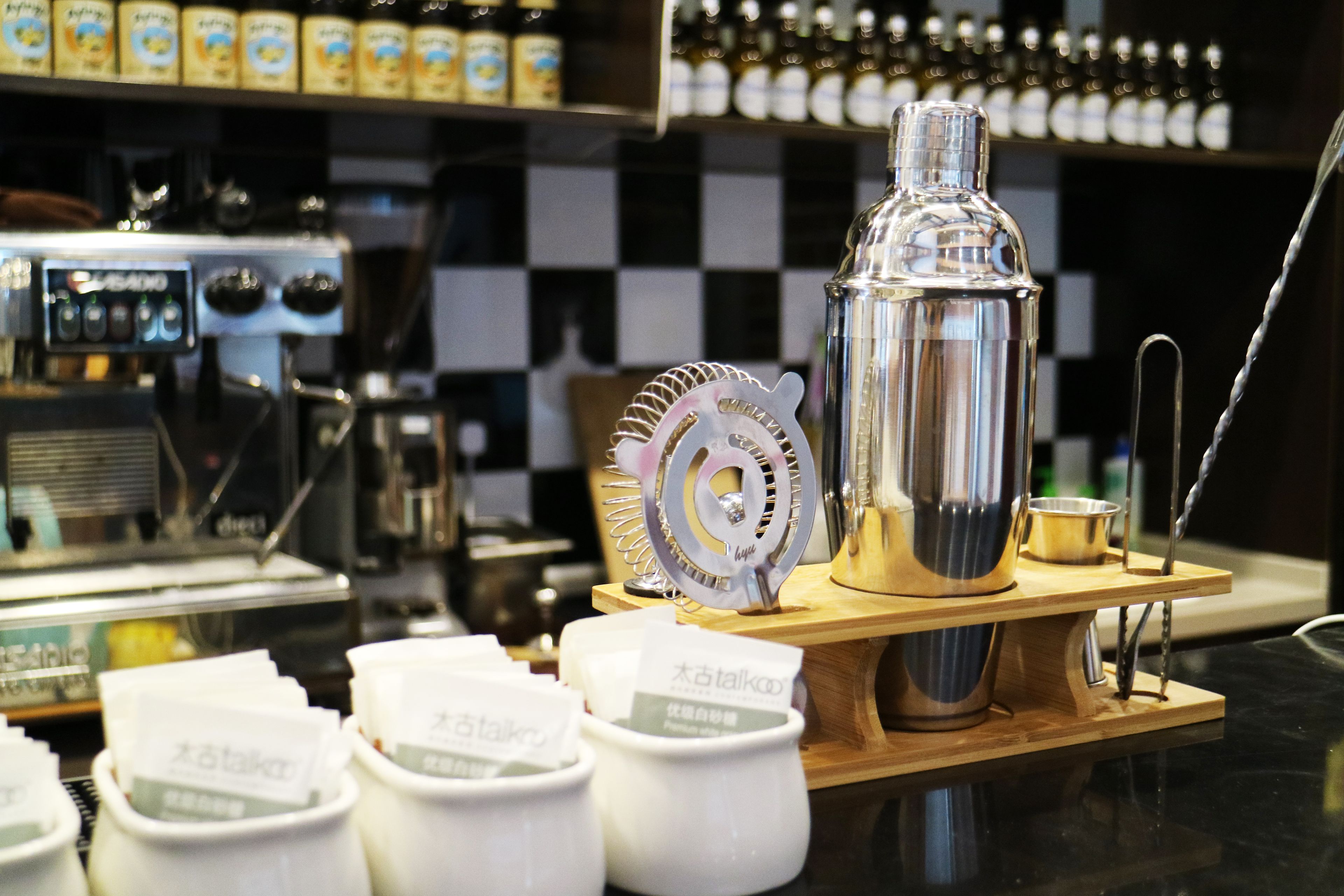 A coffee machine, a metal container, and several white cups with labels on a counter.