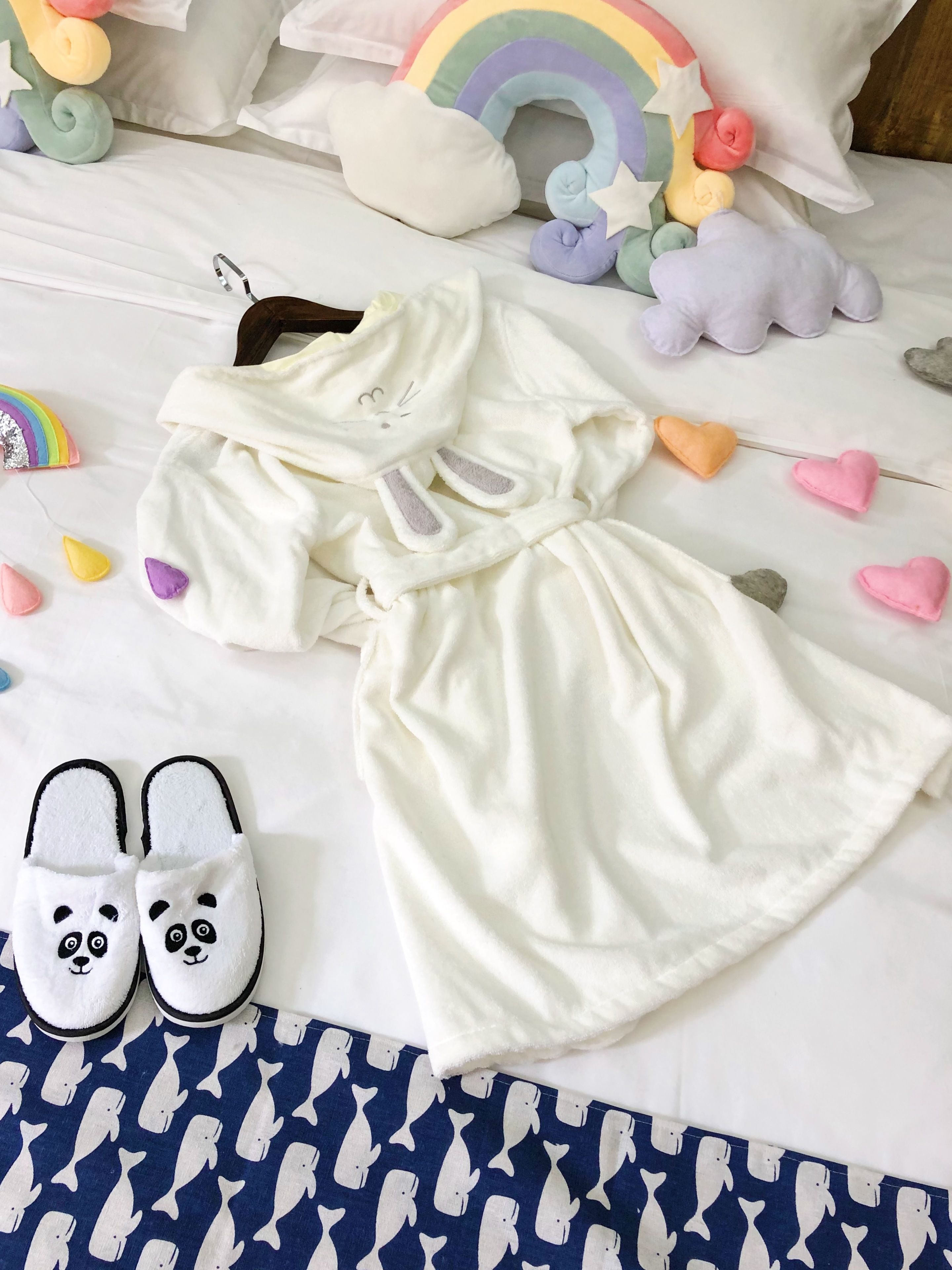 A neatly arranged bed with a white blanket, a white dress, and a pair of panda slippers.