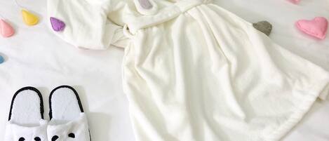 A neatly arranged bed with a white blanket, a white dress, and a pair of panda slippers.