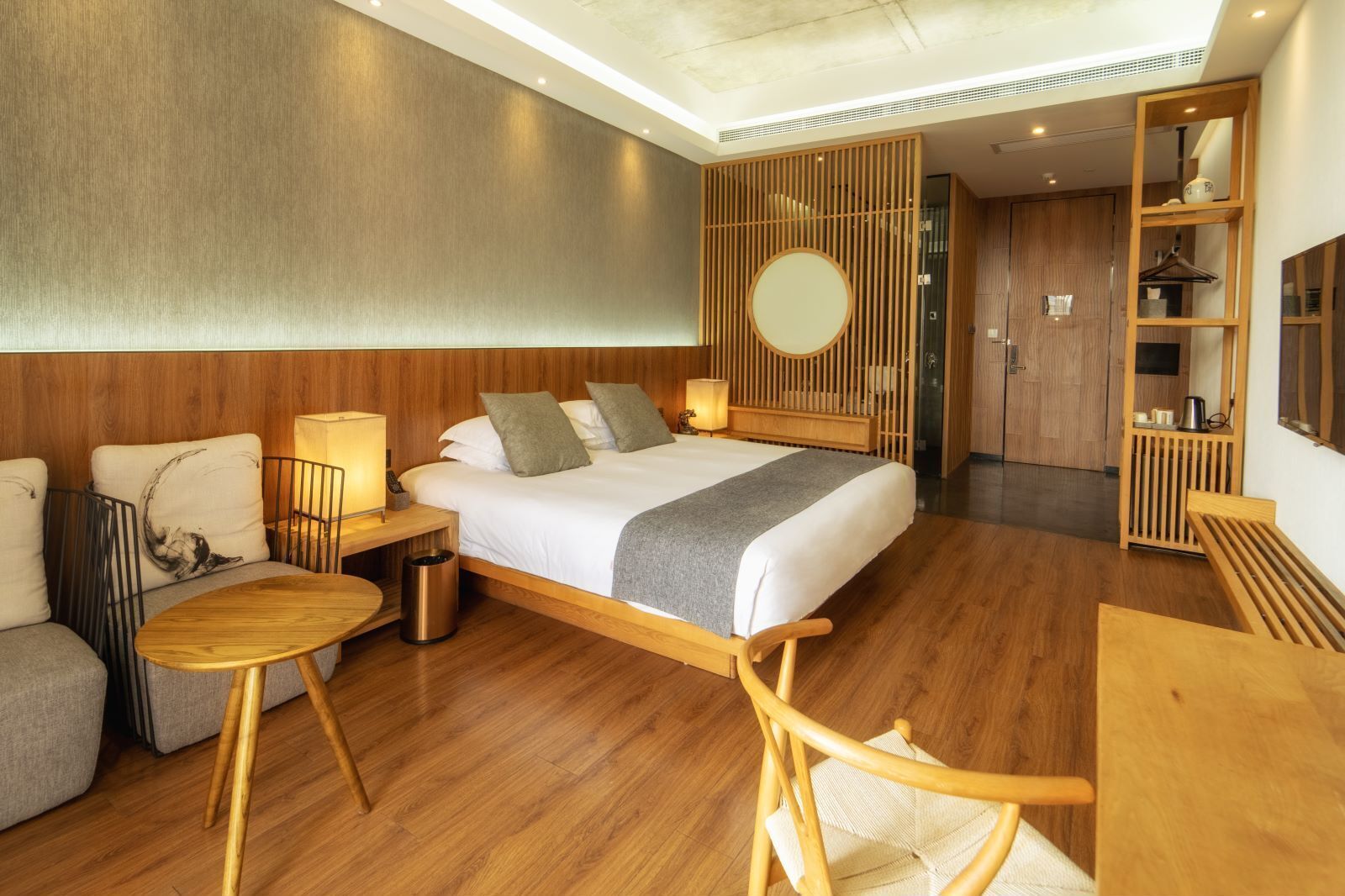 A modern hotel room with a wooden bed, a round mirror, a sofa, and a small table.
