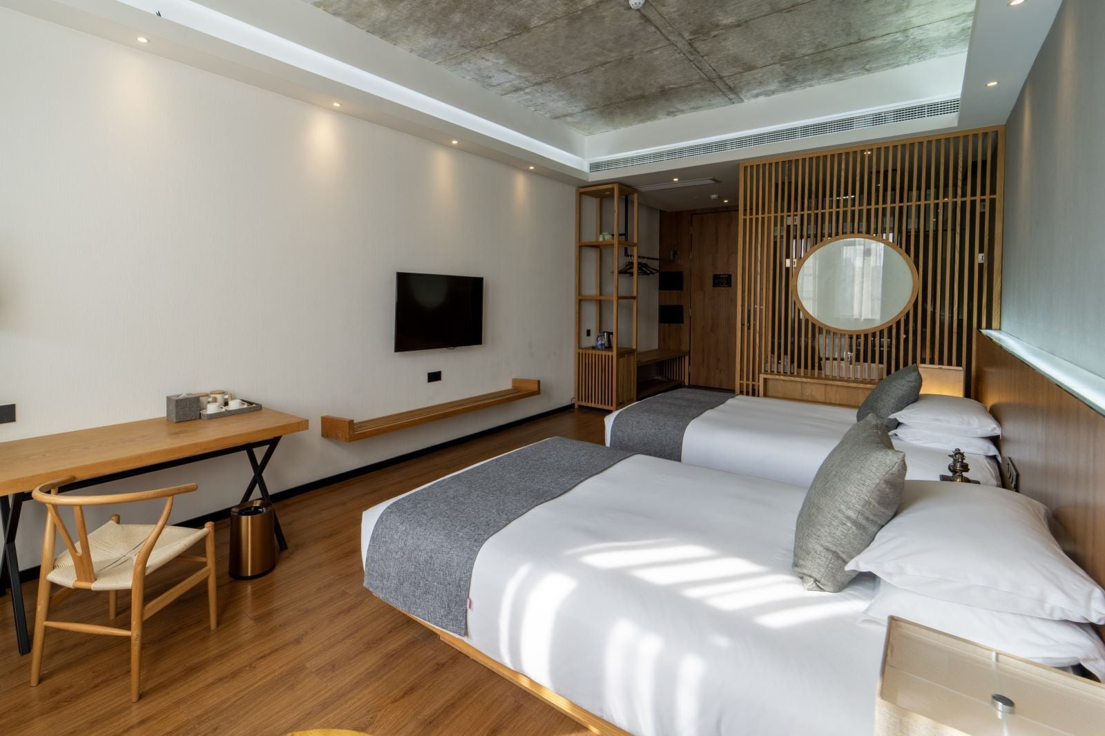 Une chambre d’hôtel moderne équipée de deux lits, d’un bureau, d’une chaise, d’une télévision et d’une cloison en bois agrémentée d’un miroir.