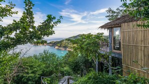 A bamboo structure with a glass enclosure overlooking a coastal area with lush greenery and a clear view of the sea.