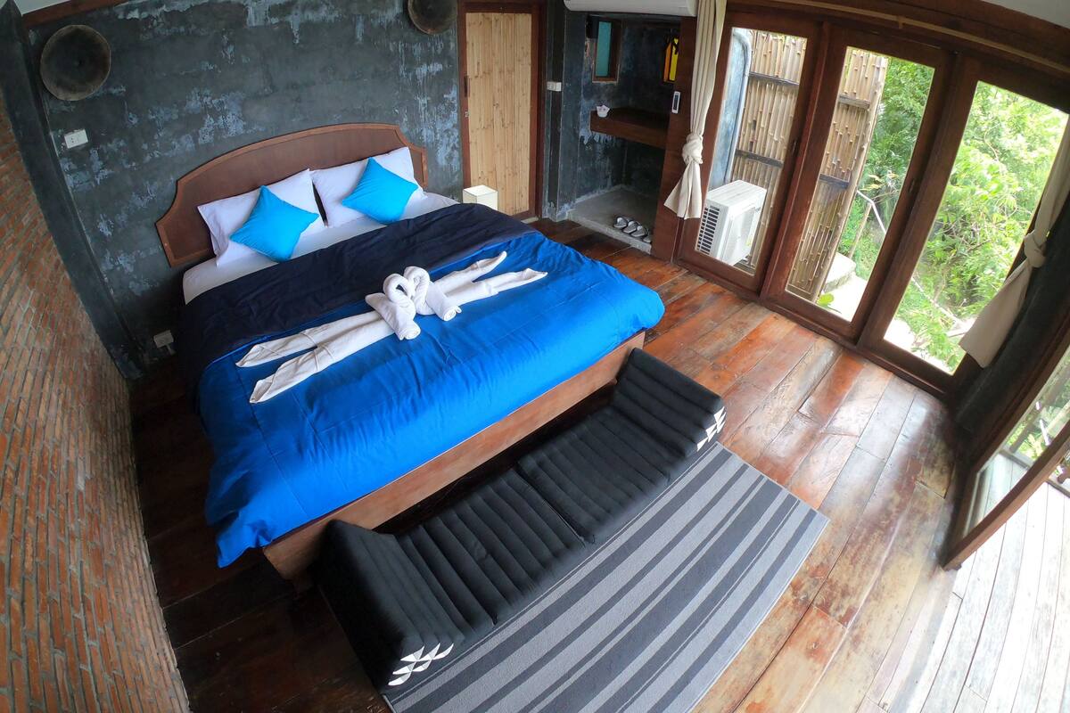 A bedroom with a bed, a bench, and a view of greenery.