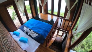A bedroom with a bed, pillows, and a view of greenery through large windows.