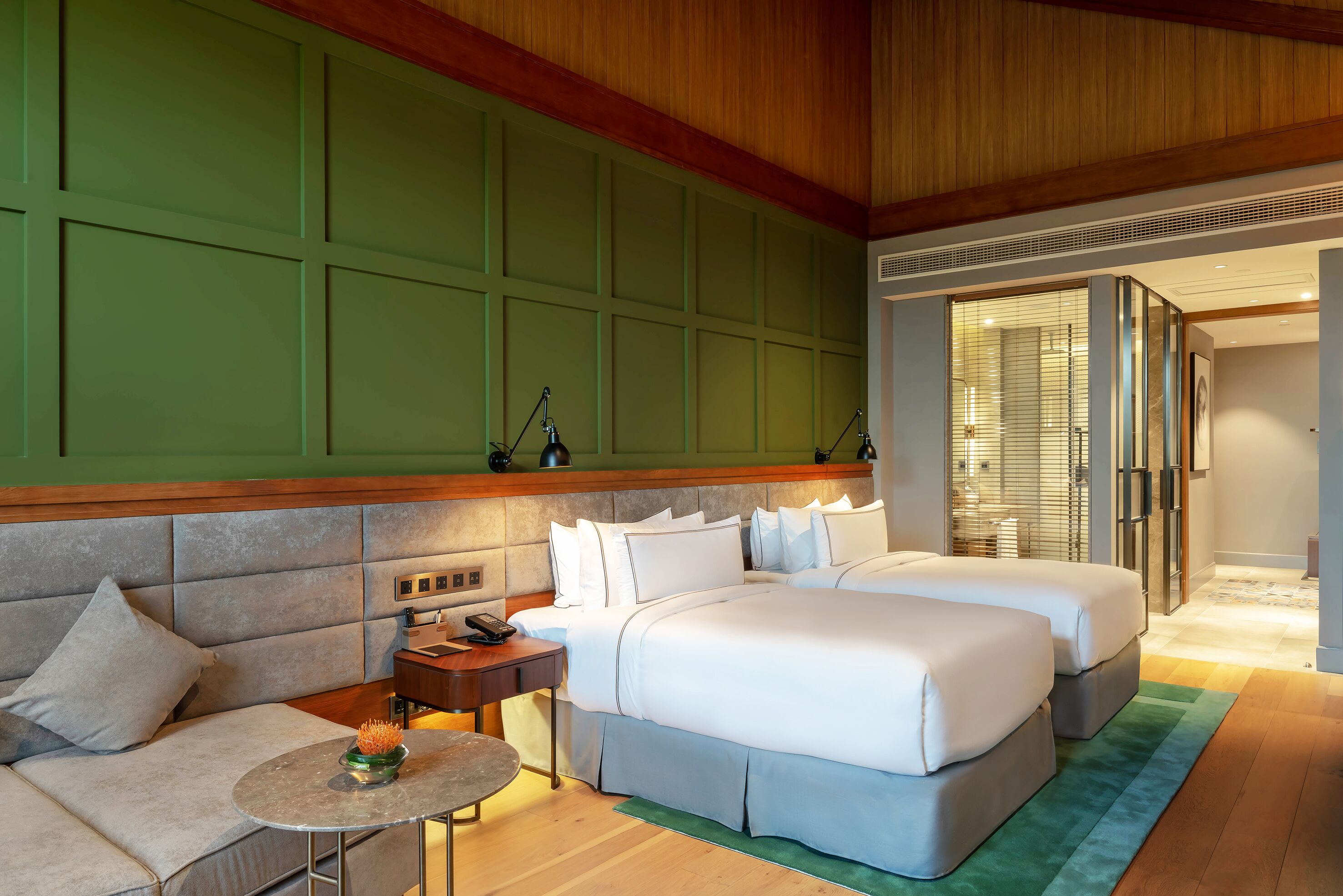 A hotel room with a large bed, a sofa, a small table, and a green wall panel.