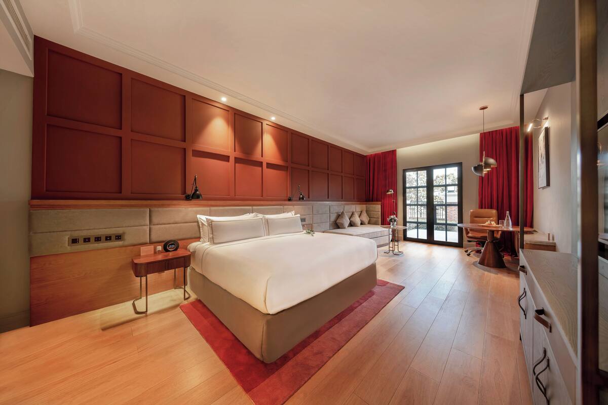 A spacious bedroom with a large bed, a wooden headboard, a bedside table, and a red accent wall.