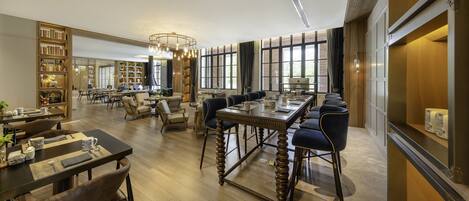 A spacious hotel lobby with a central seating area, a bookshelf, and a large window providing natural light.