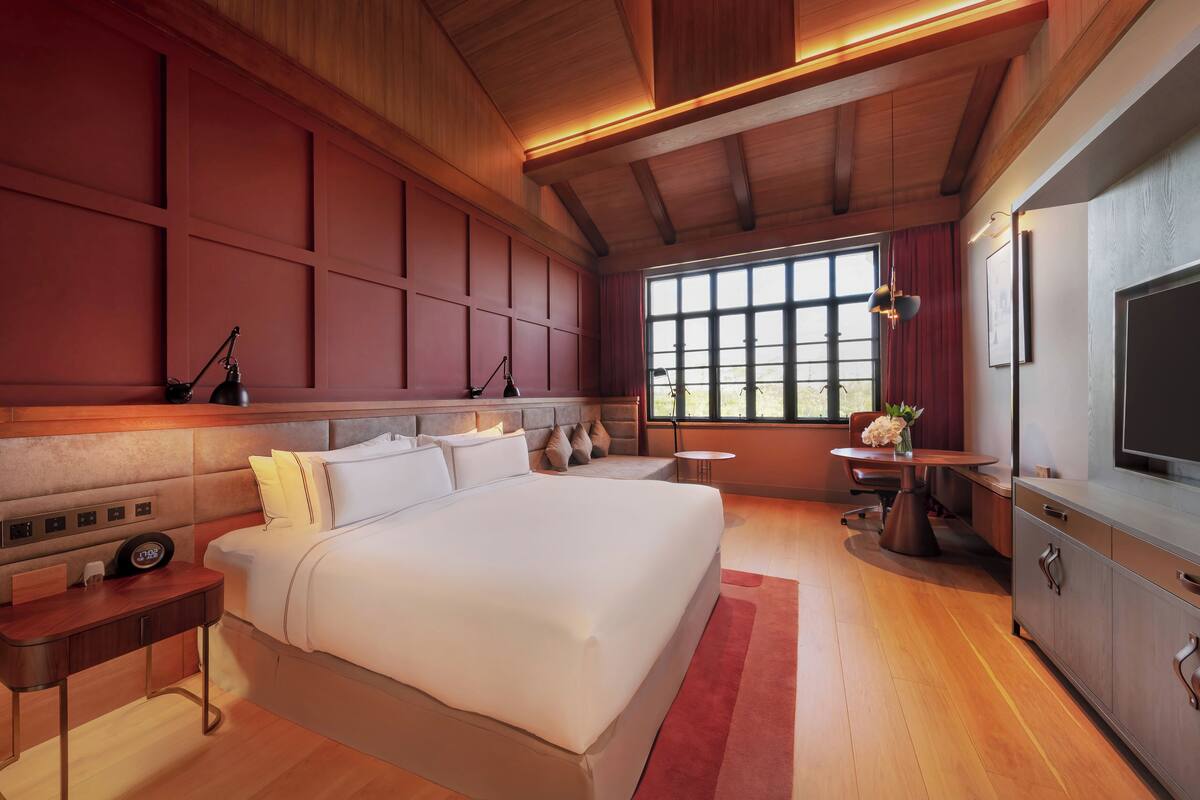 A modern bedroom with a large bed, bedside tables, a desk, a chair, a TV, and a window with curtains.