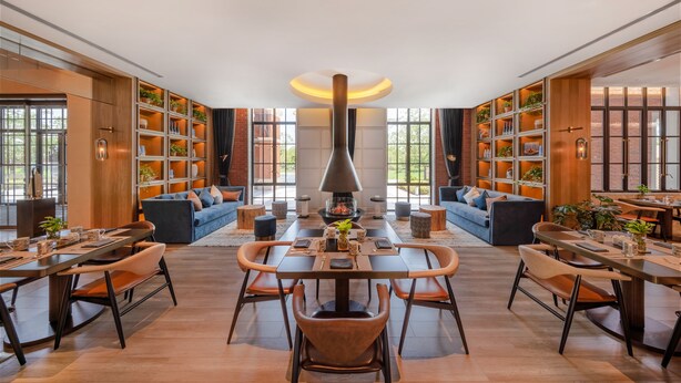 A spacious lounge area with a central fireplace, comfortable seating, and a large bookshelf filled with books and plants. - Melia Shanghai Parkside (Shanghai)