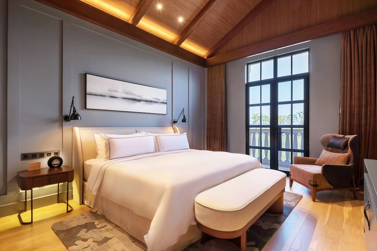 A modern bedroom with a large bed, bedside tables, a chair, and a large window.