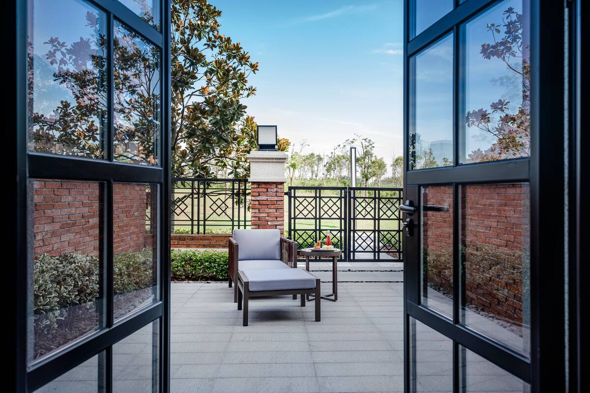 An outdoor patio with a cushioned chair and a table, a brick wall, and a metal fence.