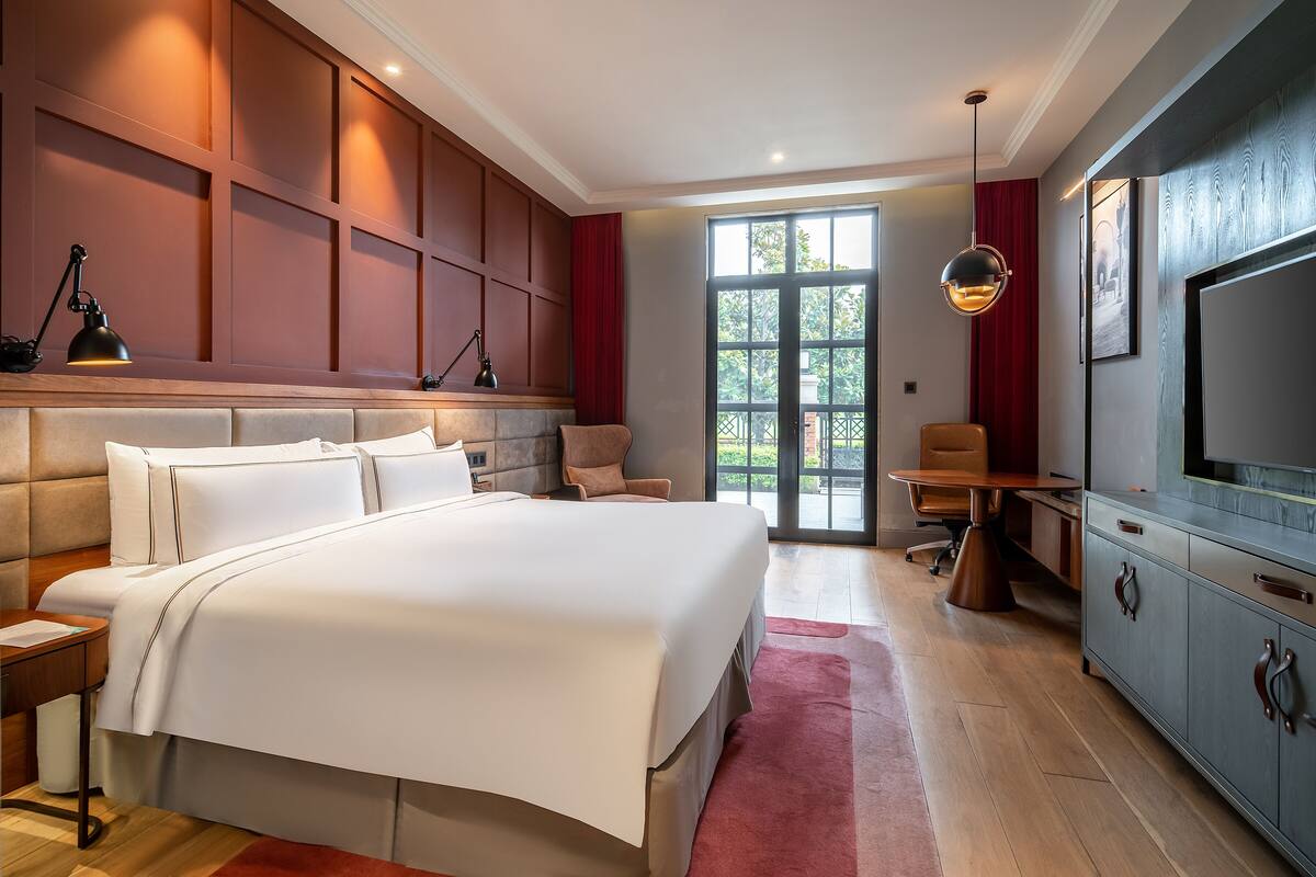 A modern hotel room with a large bed, a desk, and a television.