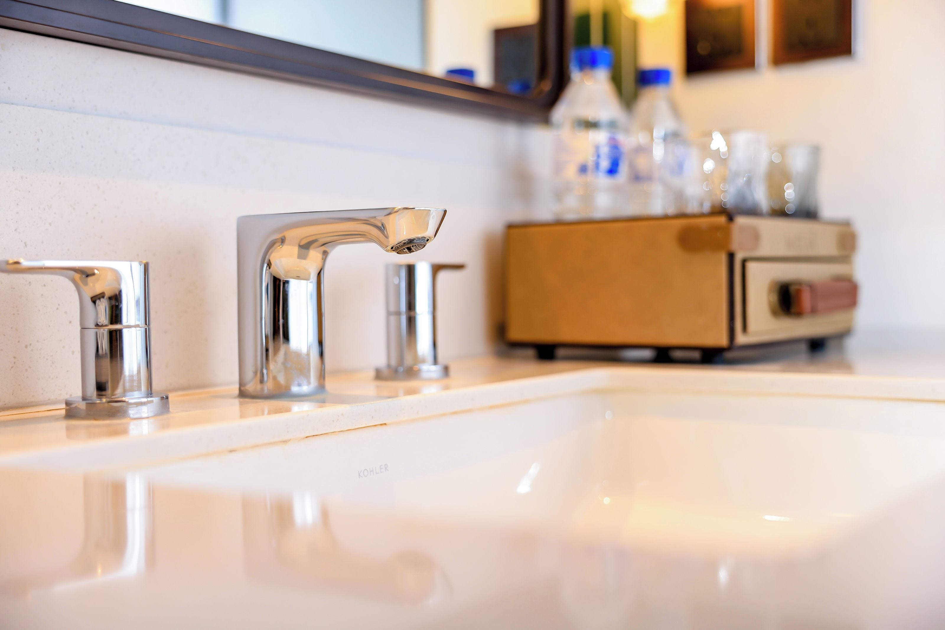 Une salle de bain avec un lavabo blanc, deux robinets en chrome et un meuble en bois contenant des bouteilles.