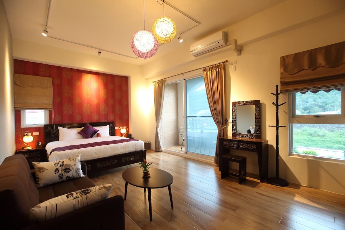 Habitación de hotel con cama, sofá, una mesita, un espejo y vistas al exterior.