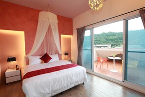 A bedroom with a large bed, a nightstand, a bedside lamp, a canopy bed, a balcony with chairs, and a view of the sea.