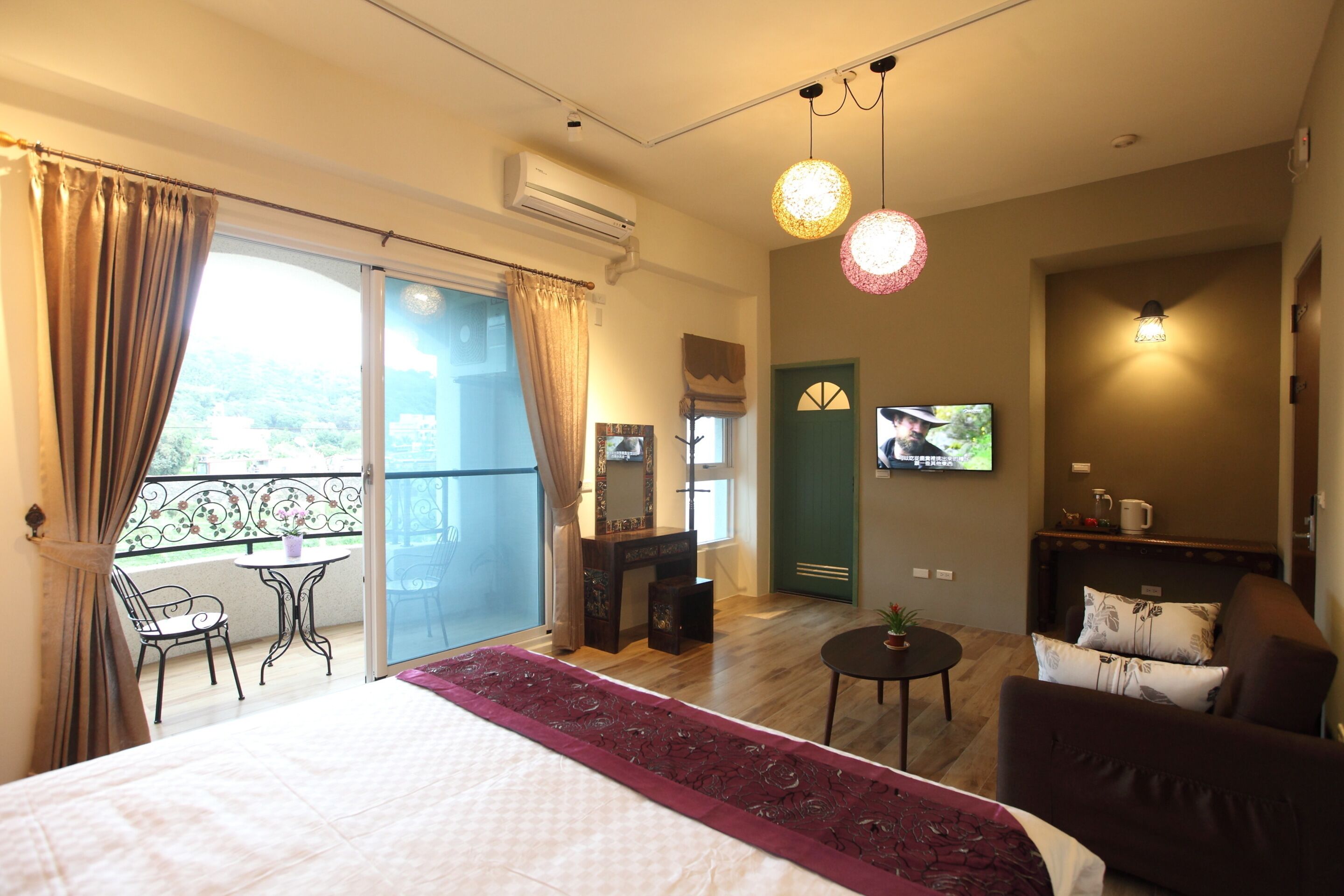 A hotel room with a bed, a balcony with a chair, a small table, a TV, and a sofa.