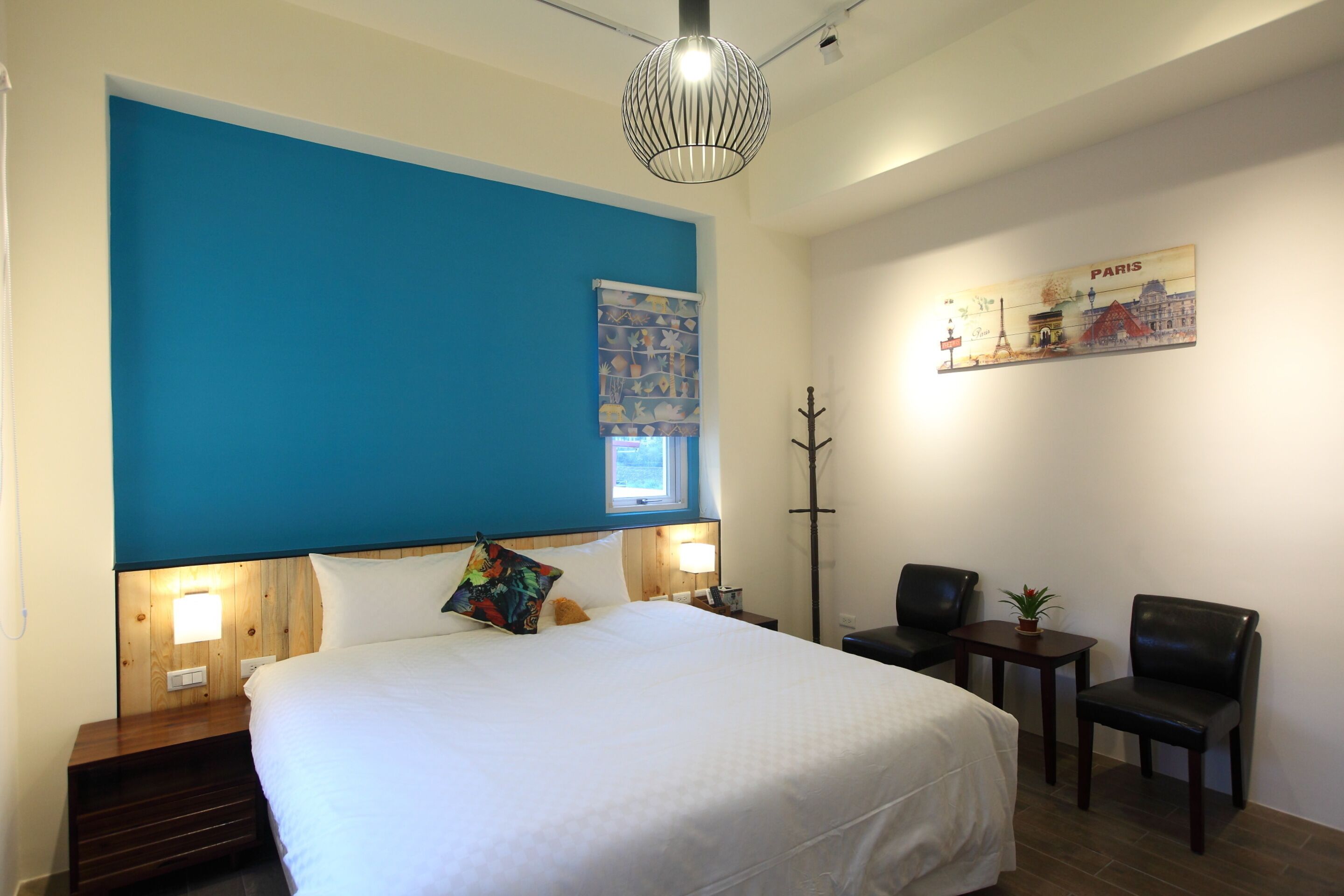 A hotel room with a large bed, a nightstand, a desk with two chairs, a lamp, and a wall decoration.
