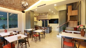 Uma sala de jantar moderna com várias mesas e cadeiras, uma cozinha ao fundo e uma escada que dá para um andar superior.