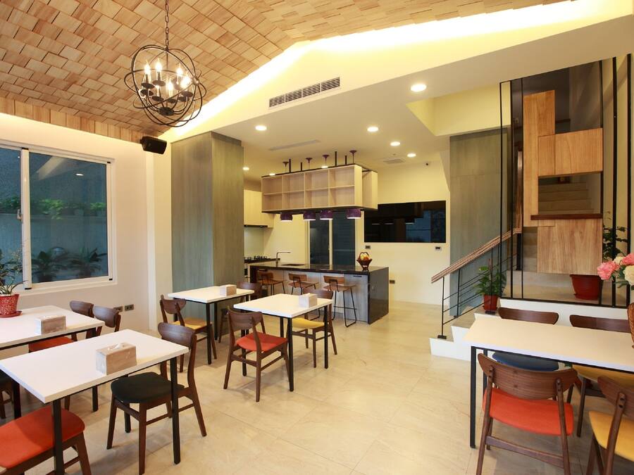 A modern dining area with multiple tables and chairs, a kitchen in the background, and a staircase leading to an upper level.