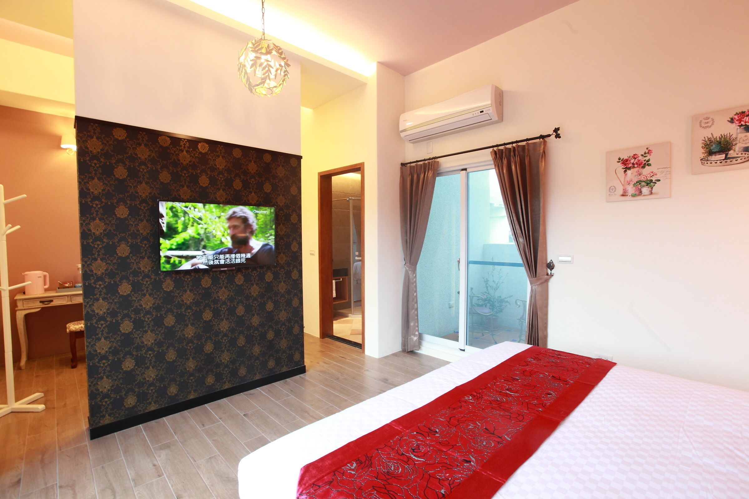 Une chambre d’hôtel équipée d’un lit, d’un téléviseur fixé au mur, d’un appareil de climatisation et d’une porte-fenêtre coulissante donnant sur un balcon.