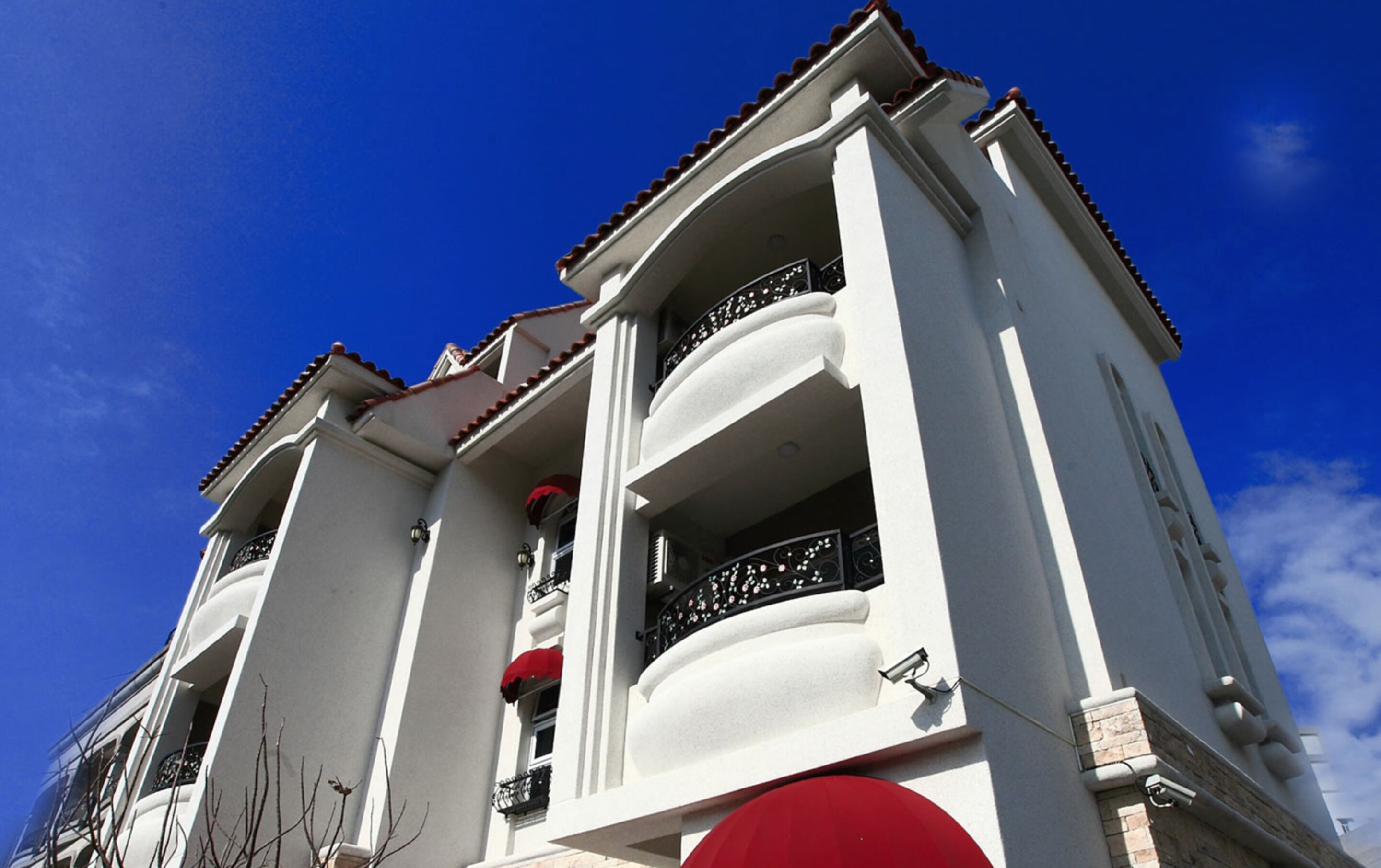 Un immeuble à plusieurs étages, doté d’une façade blanche, de touches de couleur rouge et de balcons avec des garde-corps noirs.