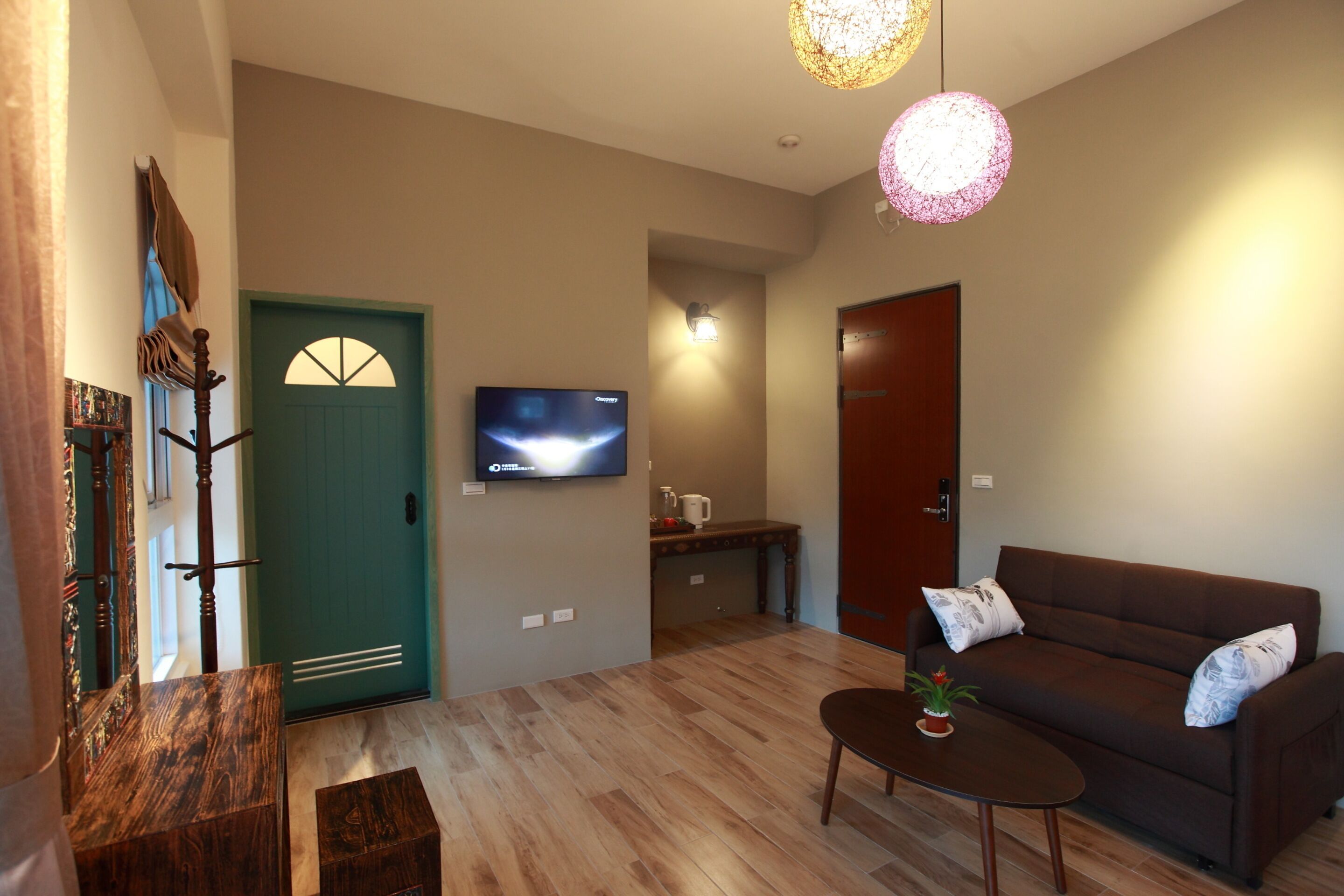 Una sala de estar con un sofá marrón, una mesa de centro, un televisor montado en la pared, una puerta de madera y una escalera.