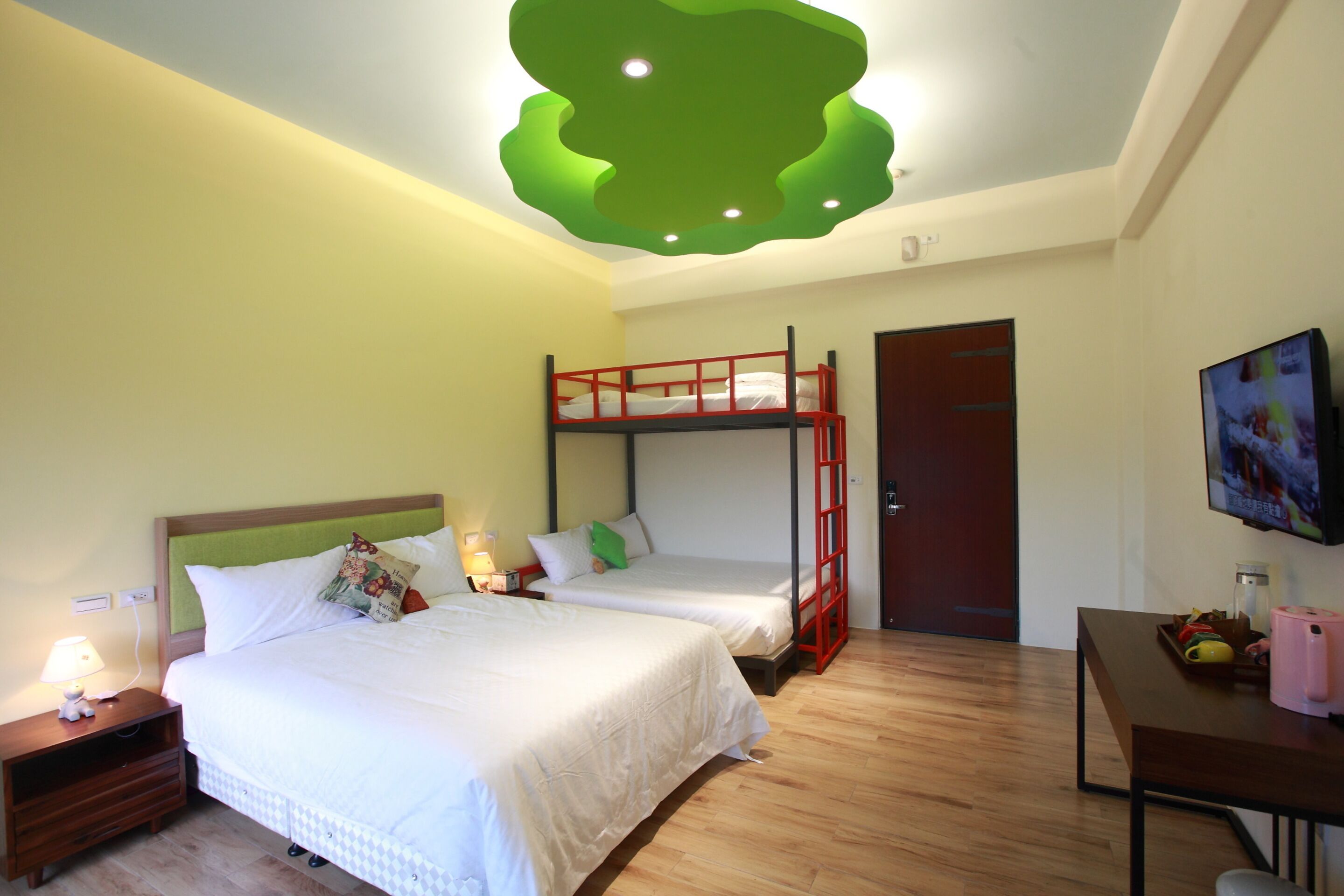 A hotel room with two beds, a bunk bed, a desk, a television, and a green ceiling design.