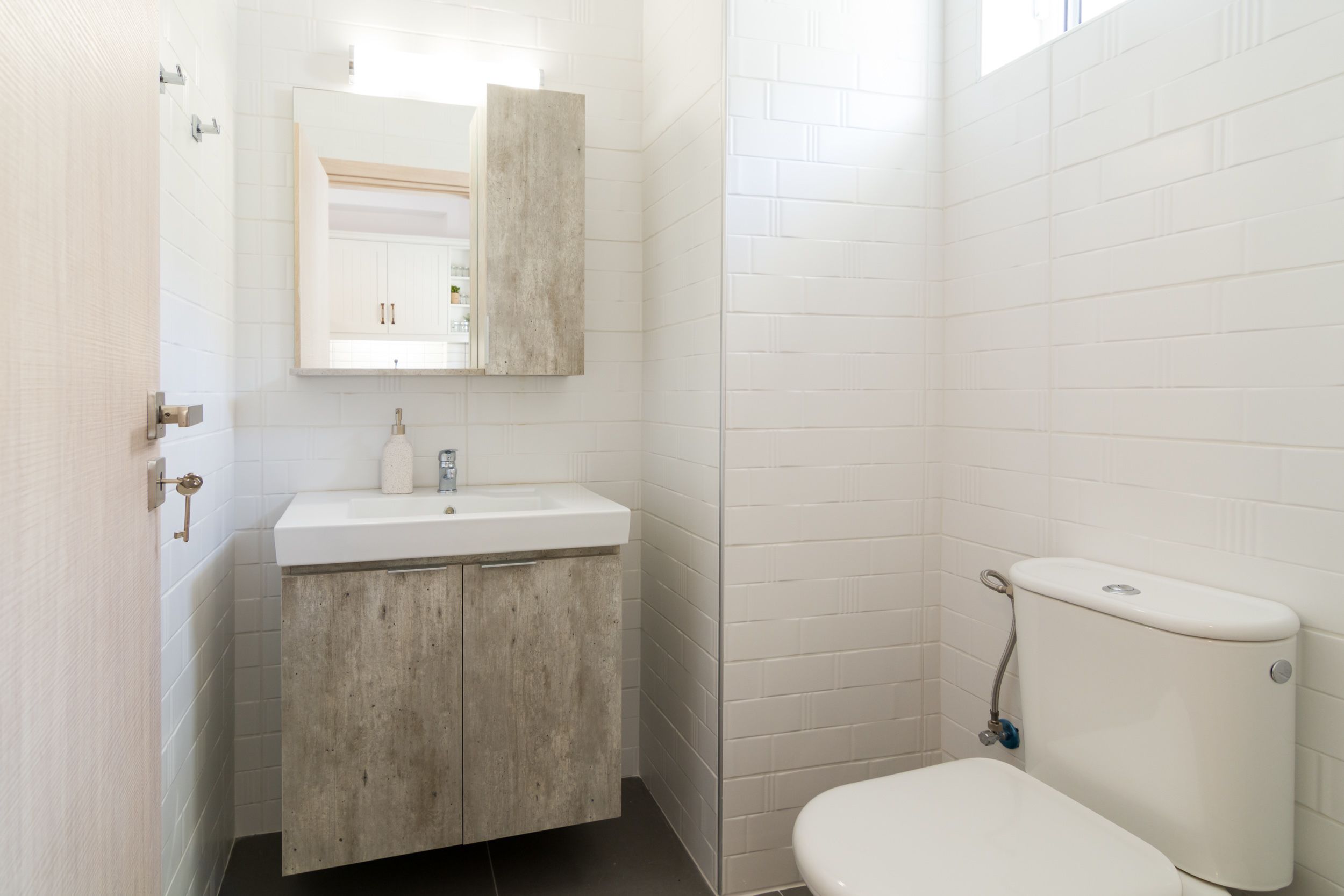 Une salle de bain avec des murs recouverts de carreaux blancs, un lavabo blanc et des toilettes.
